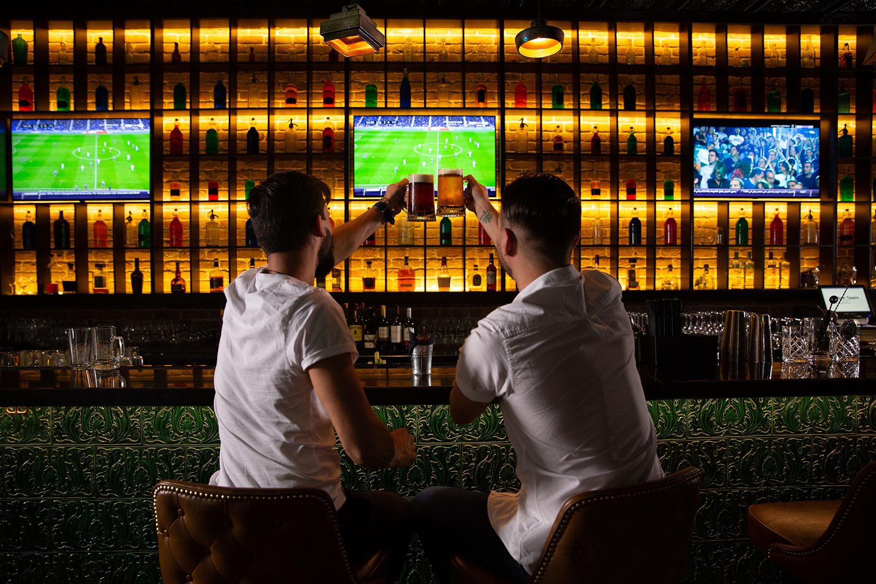 رجال يهتفون في البار أثناء مشاهدة كرة القدم في الخلفية