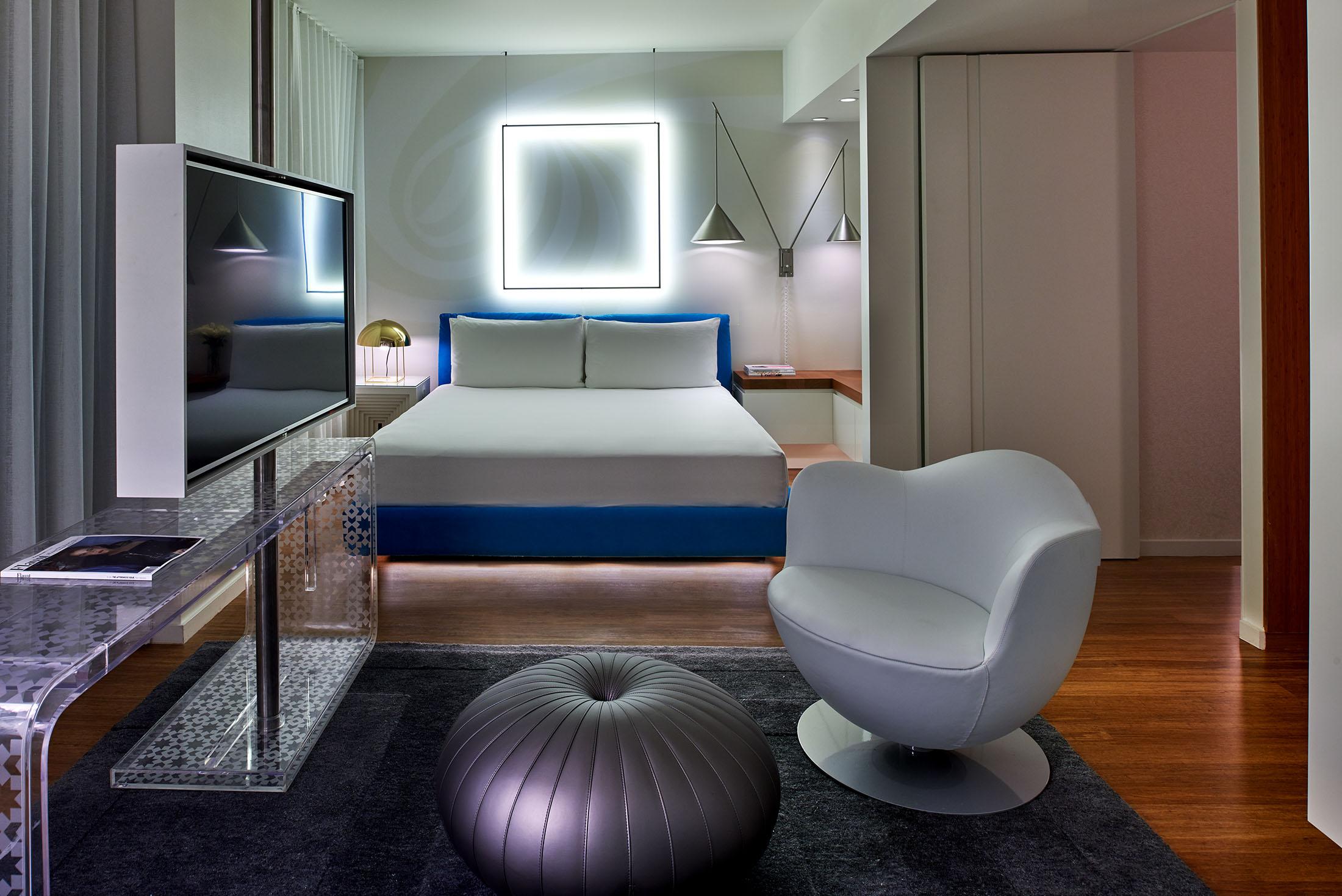 غرفة فندق بإضاءة مربعة خلف السرير وكرسي في المقدمة.