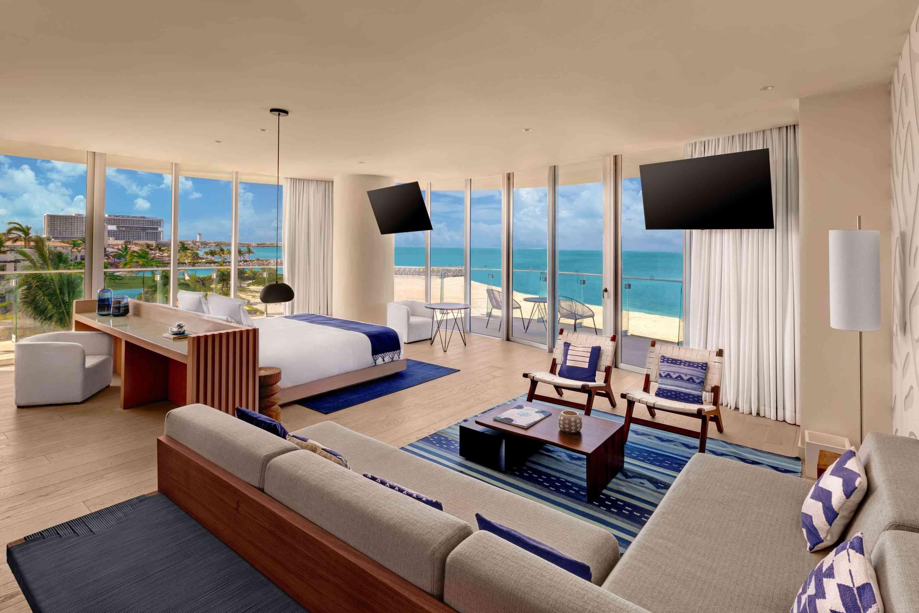 لقطة واسعة لجناح Premier Ocean Front بغرفة نوم واحدة والذي يتضمن مكتبًا ومنطقة جلوس كبيرة وجهازي تلفزيون وسرير وشرفة مطلة على المحيط